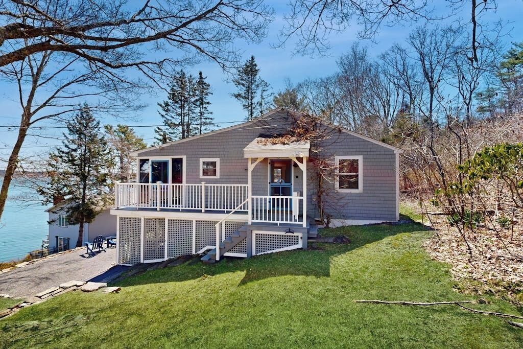 A two-story house with a balcony, a deck, and a view of a lake.