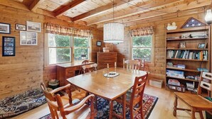 Un interior de fusta amb taula de dinar, cadires, un lampadari i una prestatgeria.