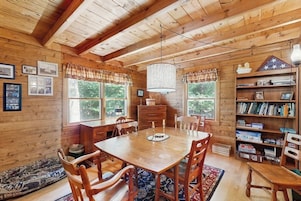 Un interior de madera con una mesa de comedor, sillas, una araña y una estantería.