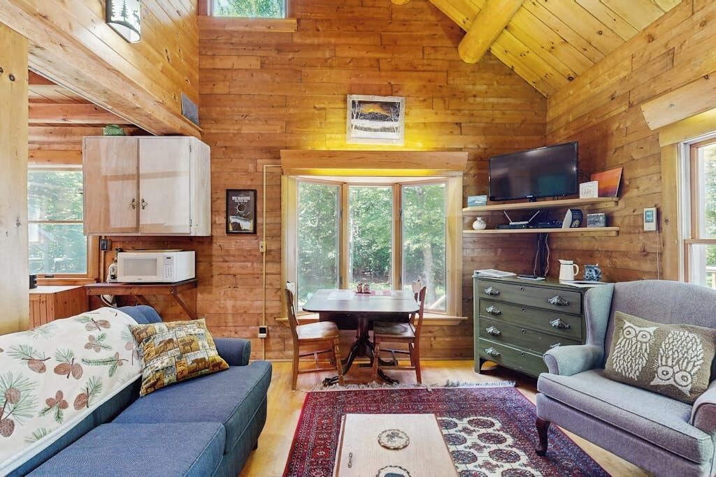 Een interieur van een blokhut met een eettafel, stoelen, een bank, een televisie en een kast.