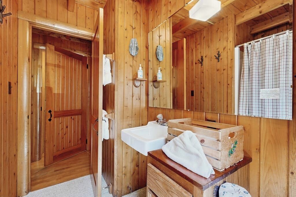 Baño de cabaña de madera con lavamanos, espejo y repisas de madera.