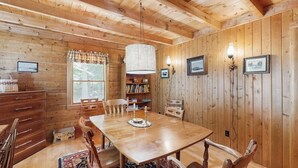Una habitació amb panells de fusta, taula de dinar, cadires, una prestatgeria i làmpades penjades a la paret.