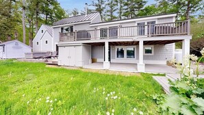 A two-story house with a balcony, a covered porch, and a garage. - Stunning Riverfront Home, hot Tub, Bbq, and Washer & Dryer (Edgecomb)