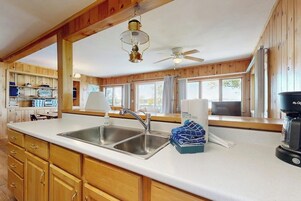 A kitchen with wooden cabinets, a double sink, a ceiling fan, and a coffee maker.