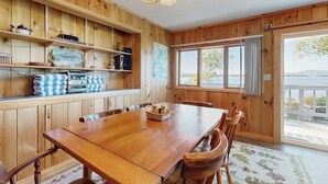 A wooden interior with a dining table, chairs, shelves with kitchen items, and a large window. - Lakefront Home With Private Dock, Mooring, Pebble Beach, Grill, & Firepit (Greenville)