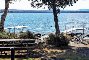 A lakeside view with a wooden dock, picnic tables, and a rocky shoreline.