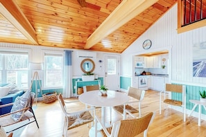 Ein gemütliches Interieur mit Holzbalkendecke, einem Essbereich mit rundem Tisch und einer Küche mit weißen Schränken.