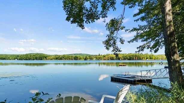 Un cadre paisible au bord d’un lac, avec un quai, une table et deux chaises Adirondack.