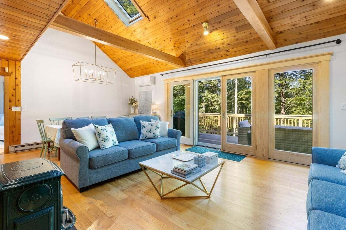 A cozy living room with a blue sofa, wooden flooring, a coffee table, and a large sliding glass door leading to an outdoor deck.