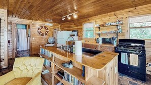 L’intérieur d’un chalet en bois comprend un coin cuisine, une table à manger et un fauteuil jaune.
