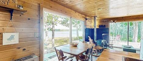 A wooden cabin with a dining area, a fireplace, and large windows overlooking a natural landscape.