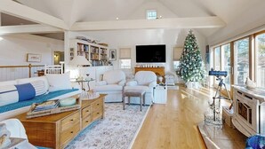Uma sala de estar espaçosa com pé direito alto, lareira,  árvore de Natal e televisão.