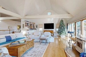 A spacious living room with a high ceiling, a fireplace, a Christmas tree, and a television.
