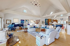 A spacious living room with a piano, sofas, and a chandelier. - The Walker (Rockport)