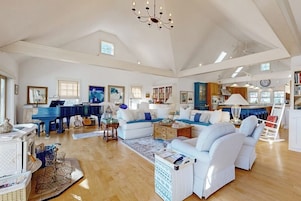 A spacious living room with a piano, sofas, and a chandelier.