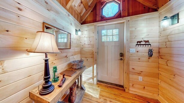 A wooden cabin interior with a lamp, a bench, a door, and a wall-mounted light fixture. - Cozy Woodsy Cabin w/ a Deck, Firepit, Gas Grill, Free Wifi, & Full Kitchen (Greenville)