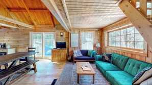 A wooden cabin interior with a dining table, sofa, and a television. - Cozy Woodsy Cabin w/ a Deck, Firepit, Gas Grill, Free Wifi, & Full Kitchen (Greenville)