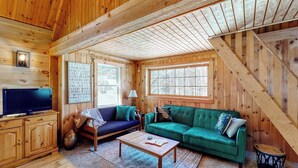 A wooden cabin interior with a television, two sofas, a coffee table, and a staircase. - Cozy Woodsy Cabin w/ a Deck, Firepit, Gas Grill, Free Wifi, & Full Kitchen (Greenville)