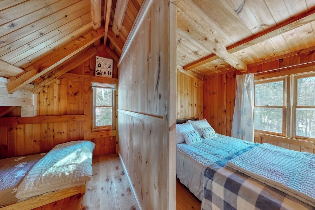 Una baita con pareti in legno, un letto a soppalco, un letto a castello e una finestra vista alberi.