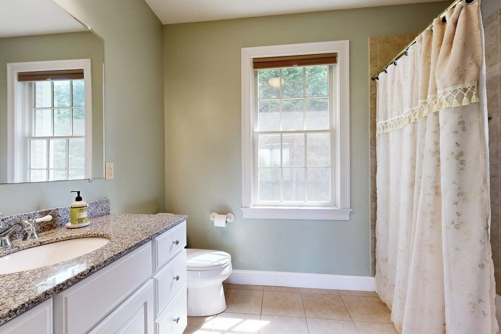 A bathroom with a sink, toilet, window, and shower curtain.