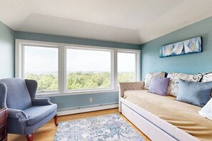 Ein Schlafzimmer mit großem Fenster, einem Bett, einem Sessel und einem Bild an der Wand.
