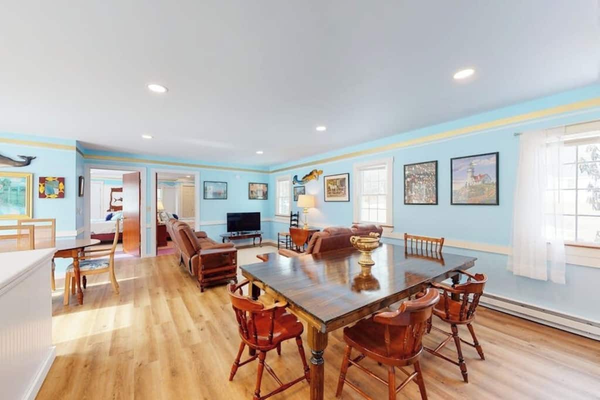 A spacious dining area with a large wooden table and chairs, a television, and a cozy seating area with a sofa and chairs.
