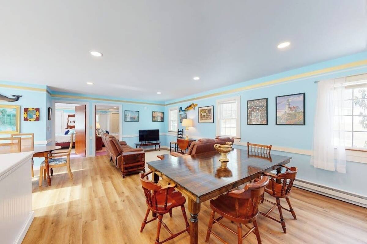 A spacious dining area with a large wooden table and chairs, a television, and a cozy seating area with a sofa and chairs.