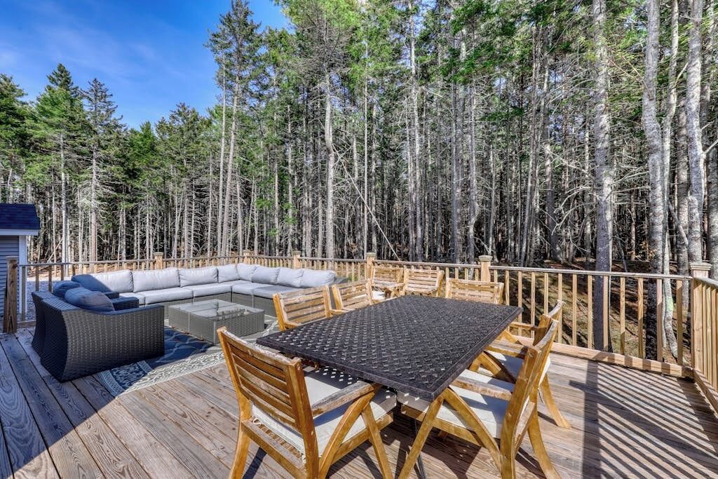 Eine Holzterrasse mit Tisch, Stühlen, einer Couch und einer kleinen Feuerstelle.