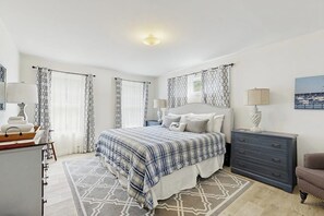 Ein Schlafzimmer mit einem Bett, Nachttischen, einer Kommode, einem Sessel und einem Bild an der Wand.