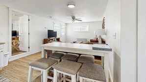 Een ruime woonkamer met een centraal eiland, zitplaatsen, een plafondventilator en een televisie.
