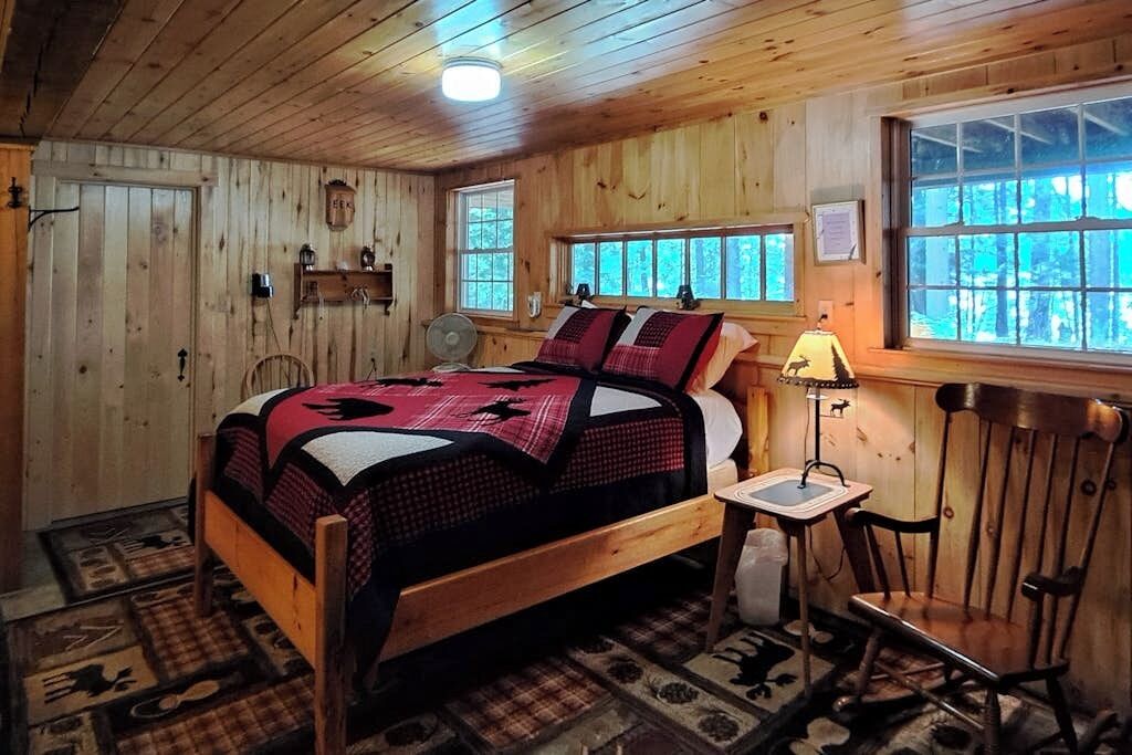 A wooden-paneled room with a bed, a table with a lamp, and a chair.