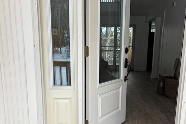 A white door with a glass panel, leading to a wooden deck with snow. - Gorgeous Oceanfront Home With Hot Tub, Modern Remodel, and Stunning Views (Wiscasset)