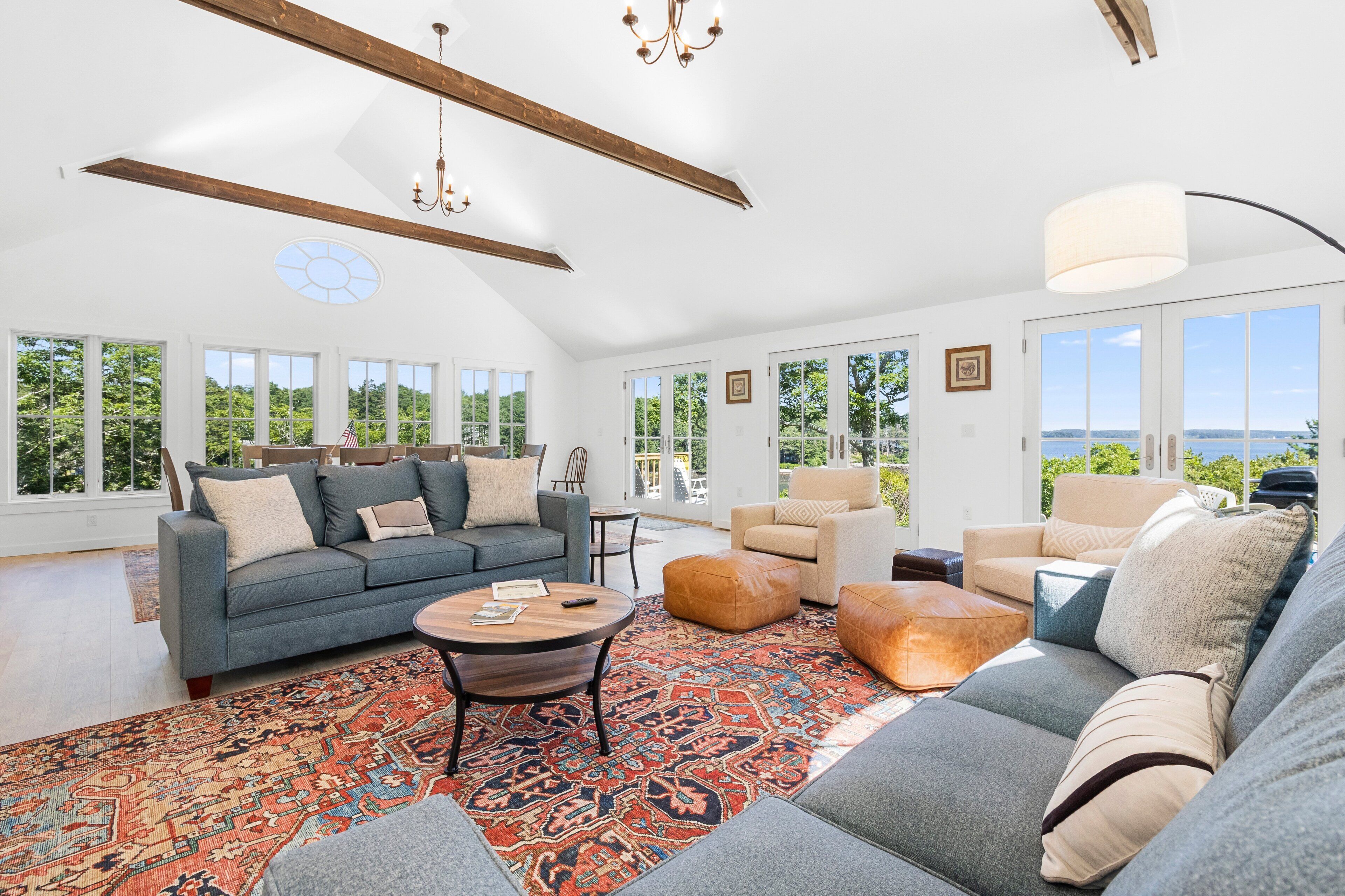 A spacious living room with a large window, a chandelier, and a patterned rug.