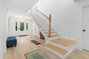 Un interior moderno con escalera de madera, paredes blancas y un banco azul.