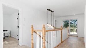 A modern interior with a wooden staircase, white railings, and pendant lighting. - Gorgeous Oceanfront Home With Hot Tub, Modern Remodel, and Stunning Views (Wiscasset)