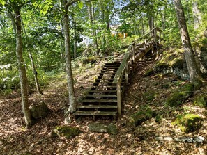 Eine Holztreppe in einem bewaldeten Gebiet mit Bäumen und einem Haus im Hintergrund.