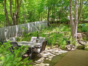 A wooden deck with a table and chairs, surrounded by greenery and trees. - Two-level Unit w/ Patio, Deck, Firepit, Private Washer/ Dryer, and Free Wifi (Seal Harbor)