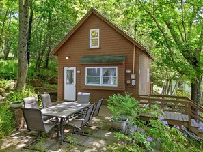 A wooden cabin with a patio, outdoor seating, and surrounding greenery. - Two-level Unit w/ Patio, Deck, Firepit, Private Washer/ Dryer, and Free Wifi (Seal Harbor)