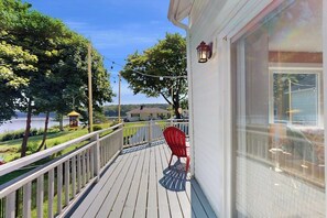 Une terrasse en bois avec une balustrade, une chaise rouge et une lanterne fixée au mur extérieur d’un bâtiment.