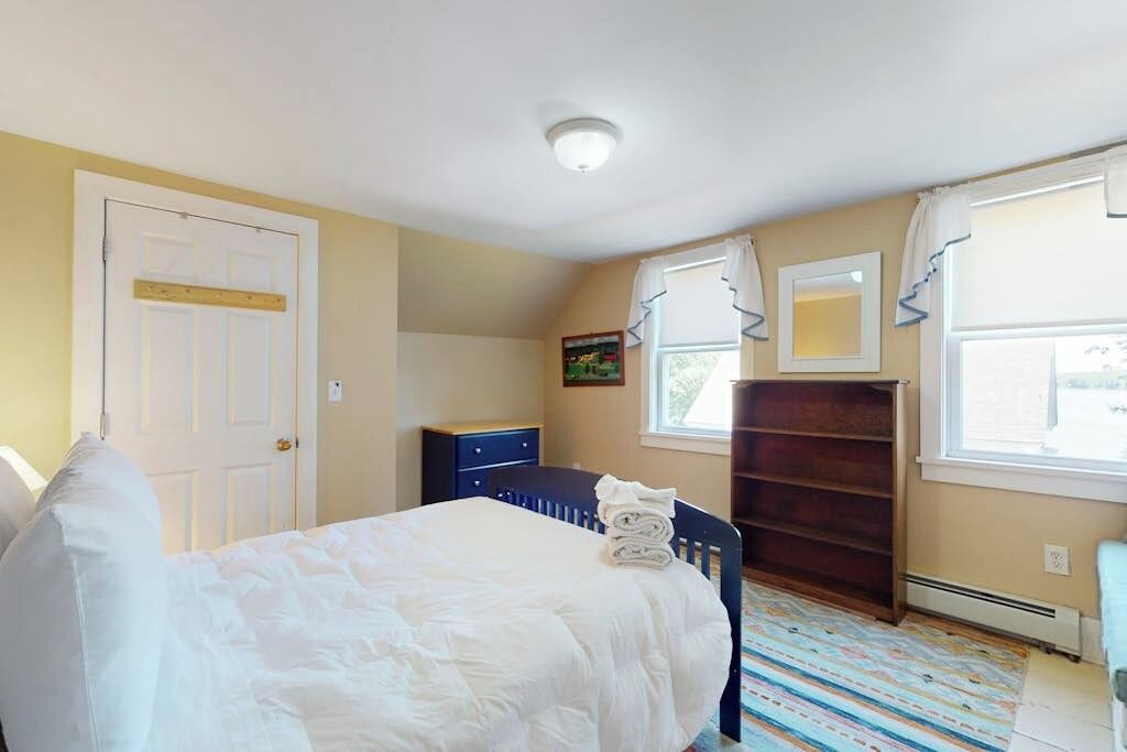 A bedroom with a bed, a dresser, a window with curtains, and a door.