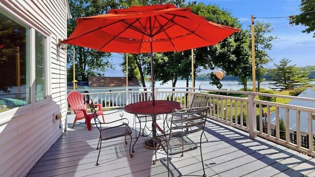 A deck with a table and chairs, a red umbrella, and a view of a lake. - Charming Cape-style House With Panoramic River Views and Modern Amenities (Bath)