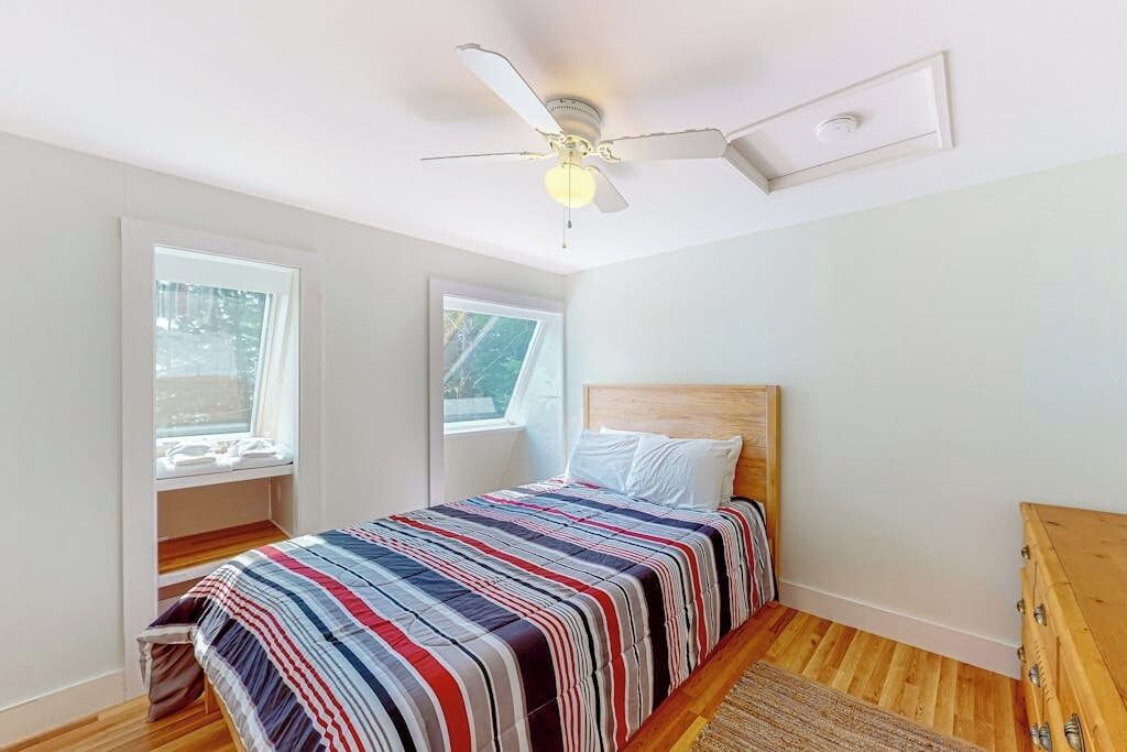 A bedroom with a bed, a ceiling fan, and two windows.
