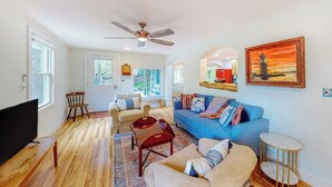Ein Wohnzimmer mit blauem Sofa, Fernseher, Holzboden, Deckenventilator und einem Gemälde eines Leuchtturms.