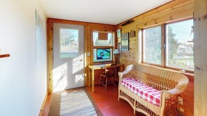 A cozy room with a wicker sofa, a desk with a computer, and large windows. - Bayfront House on Port Clyde Harbor With Views, hot Tub, Beach Access (Port Clyde)