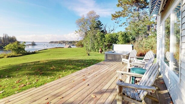 A wooden deck with outdoor seating, overlooking a body of water and a grassy area. - Bayfront House on Port Clyde Harbor With Views, hot Tub, Beach Access (Port Clyde)