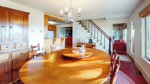 A dining area with a wooden table, chairs, a chandelier, and a staircase leading to another level. - Bayfront House on Port Clyde Harbor With Views, hot Tub, Beach Access (Port Clyde)