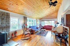 A cozy living room with a stone wall, wooden ceiling, and a fireplace. - Bayfront House on Port Clyde Harbor With Views, hot Tub, Beach Access (Port Clyde)