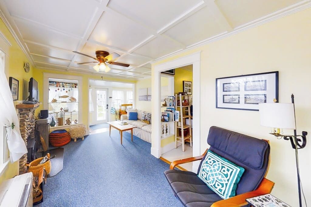 A living room with a sofa, a coffee table, a bookshelf, and a ceiling fan.