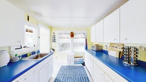 A kitchen with white cabinets, a blue countertop, a patterned rug, and a window with a view of trees. - Dog-friendly Fisher Hill Home With Patio and Wood Stove - Walk to the Harbor (Boothbay Harbor)