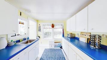 A kitchen with white cabinets, a blue countertop, a patterned rug, and a window with a view of trees.